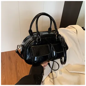 Detail of black glossy shoulder bag featuring dual front pockets and double handles