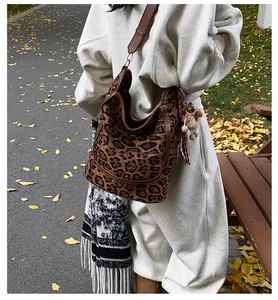 Detailed side view of leopard print tote bag with brown leather strap and plush charm