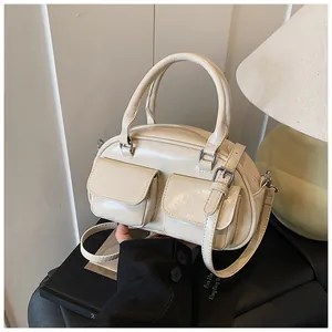Close-up of cream glossy faux leather boston bag with silver buckles and dual pockets