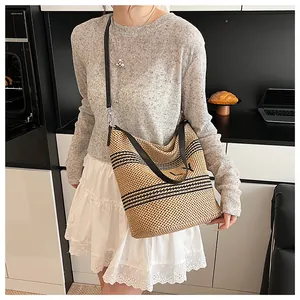 Dettaglio di una borsa tote in rafia beige intrecciata con strisce nere e tracolla in pelle