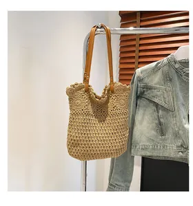 Detail of woven khaki straw tote bag with brown leather handles and hollow mesh pattern