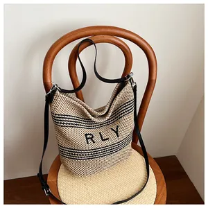 Dettaglio della borsa tote in rafia con logo RLY appesa a una sedia per un look vacanza