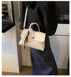 Detail of cream shoulder bag featuring silk scarf handle and golden twist lock