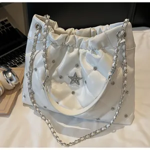 Détail du sac seau blanc matelassé avec strass étoile et chaîne argentée sur bureau