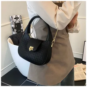 Detail of black woven crescent bag with gold chain strap and metal lock in a modern setting