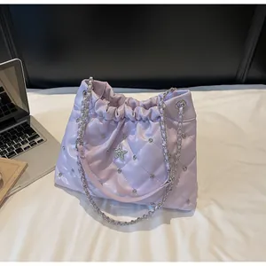 Détail du sac seau matelassé lavande avec strass et bandoulière chaîne sur le lit