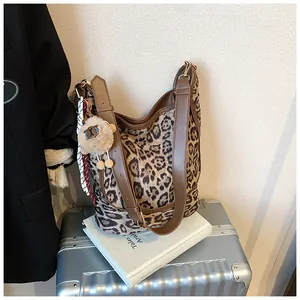 Detail of leopard print hobo bag with brown leather trim and plush charm on travel luggage