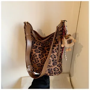 Close-up of leopard print hobo bag with brown strap and plush toy pendant detail