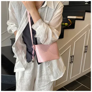 Close-up of pink woven crossbody bag with silver heart charm and textured leather