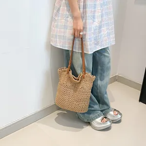 Handcrafted beige straw knit tote bag with brown leather handles worn by a model