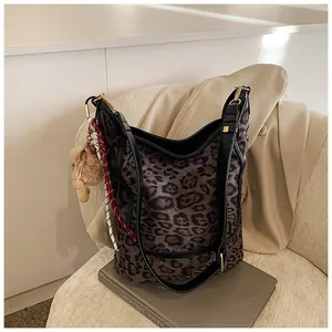 Detail of leopard print tote bag featuring black leather strap and a plush ball charm
