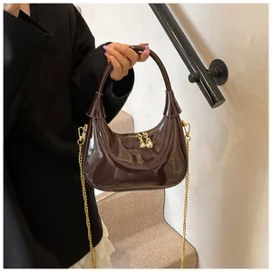 Detail of glossy dark brown patent leather bag with gold chain and ball zippers