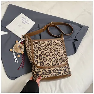 Detail of leopard print tote bag with brown trim and small plush doll charm accessory