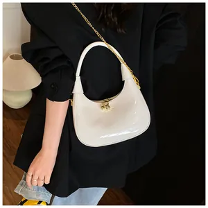 Close-up of white patent leather shoulder bag featuring gold chain and spherical zipper pulls