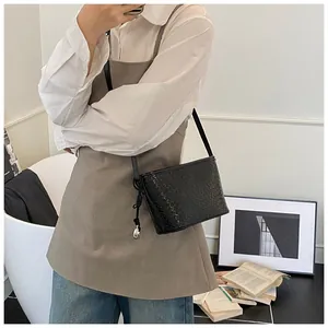 Detailed view of black woven texture crossbody bag with side ties and silver pendant
