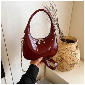Detail of dark burgundy glossy patent leather bag with gold hardware and chain strap