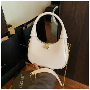 Macro detail of glossy white crescent bag with gold chain strap and spherical zipper pull