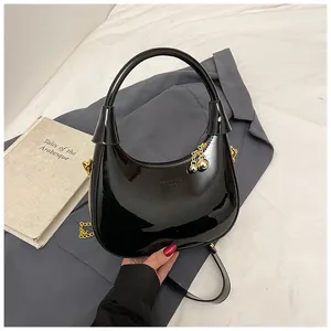 Detail of black patent leather hobo bag with gold chain strap and metal ball charm