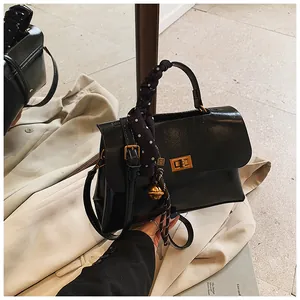 Close-up of black leather handbag featuring a gold twist lock and polka dot scarf wrap