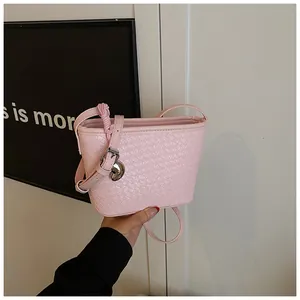 Detail of pink woven leather bucket bag featuring a silver heart charm and adjustable strap