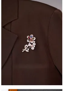 Detail of a gold double flower brooch with multicolored gemstones on a brown blazer lapel