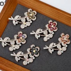 Five vintage crystal flower brooches in assorted colors on a textured display