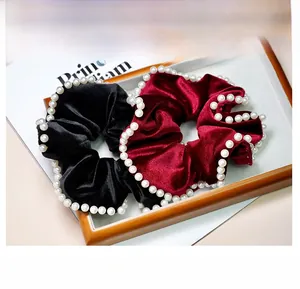 Detail of velvet pearl hair scrunchies in black and burgundy on a wooden tray