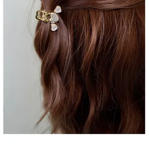Nahaufnahme einer goldenen Mini-Haarklammer mit weißen Steinchen auf braunem Haar