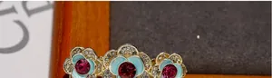 Close-up of light blue enamel rose hair clip with pink crystal and golden finish