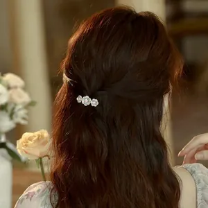 Elegant Chinese rose hair clip with green and pearl flowers worn on wavy brunette hair