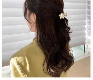 Detail of a cream acetate star-shaped hair claw with gold trim worn on long wavy hair