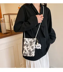 Detail view of mini cow print crossbody bag with plush charm and metal m logo decoration