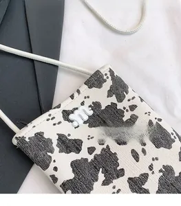 Detail of the cow print crossbody bag texture with a white m-letter logo and rope strap