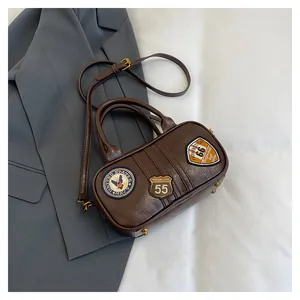 Detail of dark brown leather Boston bag featuring vintage military badges and adjustable strap