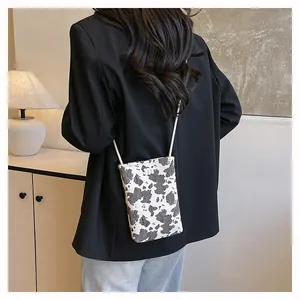 Detail of trendy cow print crossbody phone bag with slim white shoulder strap