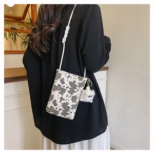Detail of cow print canvas crossbody phone bag with knot strap and plush charm