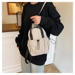 Detail of minimalist beige nylon backpack featuring side drawstring and black straps