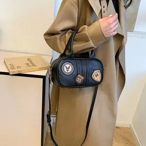 Minimalist black embroidered barrel bag with adjustable strap worn on khaki trench coat