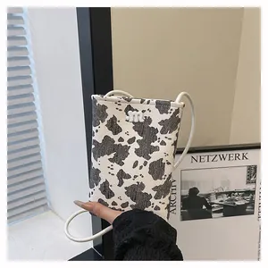 Detail of a cow print mini shoulder bag featuring a 3D white m logo and slim strap