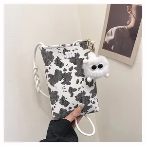 Detail of cow print crossbody bag with woven strap and plush monster charm decoration
