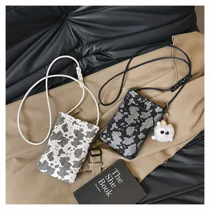 Detailed view of mini crossbody phone bags in stylish cow print with plush doll charm