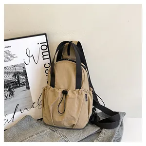 Close-up of khaki nylon backpack featuring drawstring pocket and black woven strap detail