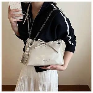 Détail du sac bandoulière blanc cassé avec nœud, chaîne en métal et breloque cadenas