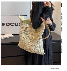 Detail of handwoven straw tote bag featuring brown leather straps and cross-stitch accents