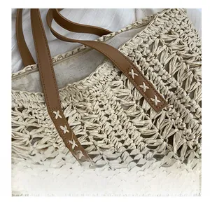 Close-up of woven straw tote bag featuring brown faux leather straps and X-shaped stitching
