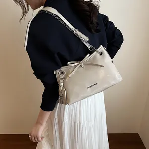 Élégant sac à bandoulière beige avec nœud et chaîne présenté dans un look professionnel