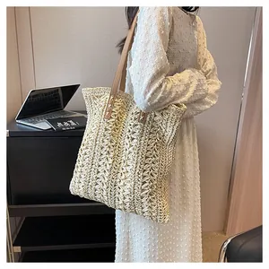 Detail of handwoven straw tote bag featuring brown leather straps and cross-stitch accents