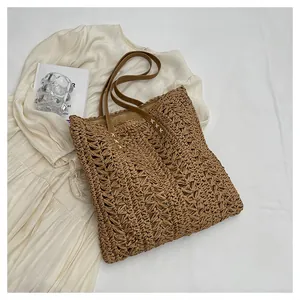 Close-up detail of a brown woven straw tote bag featuring contrast stitching on handles
