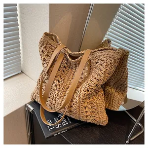 Detail view of woven straw tote bag featuring brown leather handles and white stitching