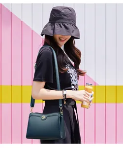 Detail of dark green pebble leather crossbody bag with golden logo and adjustable strap